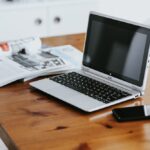 テーブルの上に、スマートフォンとシルバーのラップトップと雑誌